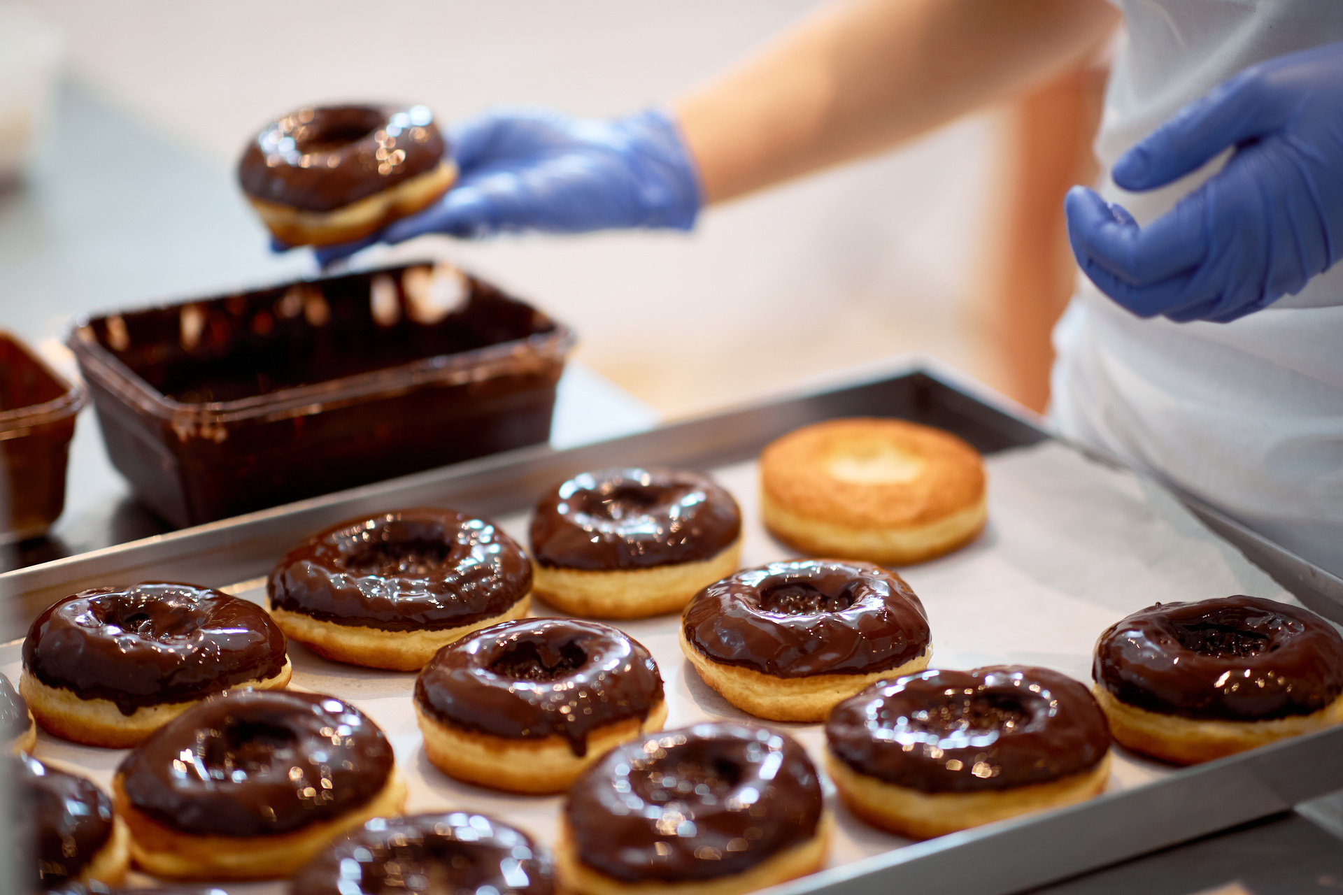 Baker arranging chocolate-glazed doughnuts on a tray