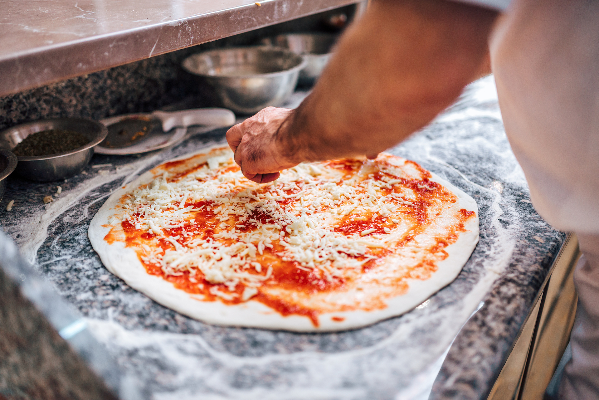 Person adding cheese to pizza dough during a hands-on pizza-making class